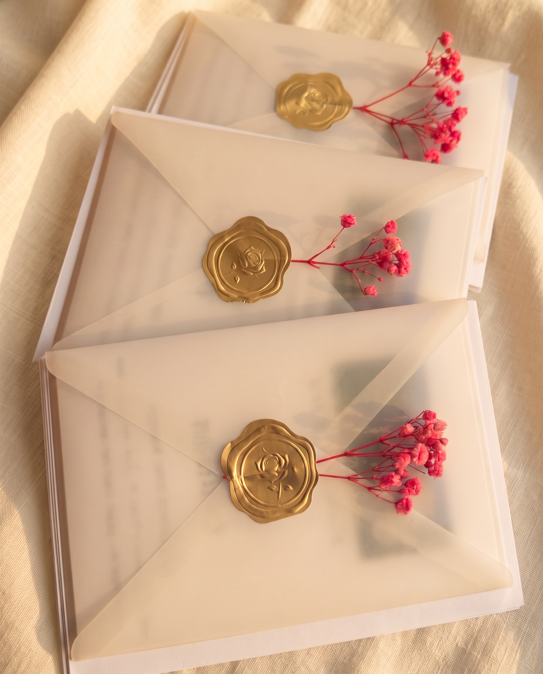 Vellum wedding invitations with gold rose wax seals and pink gypsophila on ivory linen